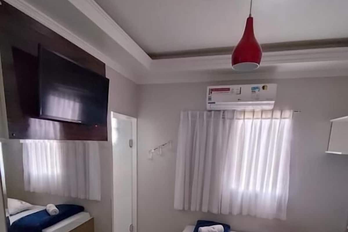 Habitación de hotel con dos camas, un televisor montado en la pared, un equipo de aire acondicionado y una lámpara colgante roja.