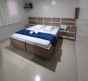 A modern bedroom with a wooden bed, a blue throw blanket, and a nightstand with a phone and a book. - Hotel M Itaquera (São Paulo)
