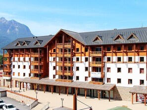 Ein mehrstöckiges Hotel mit Balkonen, einem überdachten Außenbereich und einem Berg im Hintergrund.