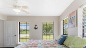 A bedroom with a floral bedspread, a ceiling fan, a door, and windows with blinds. - Matagorda-Stunning Waterfront Views-Swim Spa-Private Pier-Relax (Matagorda)