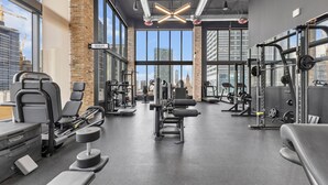 Ett gym med olika typer av träningsutrustning, stora fönster och utsikt över stadens silhuett.