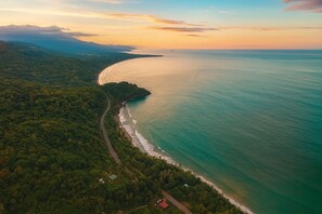 An aerial view of a coastal area with a road curving along the shoreline, surrounded by dense green forest. - Casa de Luna Villa with Ocean View (Uvita)