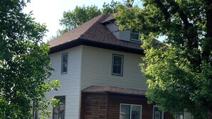 Une maison à deux étages avec un porche en bois à l’avant et une petite terrasse.