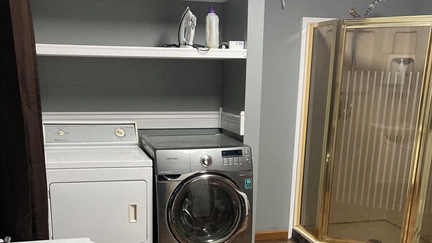 Une petite buanderie équipée d’un lave-linge et d’un sèche-linge à chargement frontal, d’un évier et d’un espace douche.