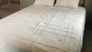 Una cama con cabecera de madera y ropa de cama blanca en una habitación con pared texturizada y suelo alfombrado.
