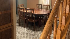 Une salle à manger avec une table et des chaises en bois, un lustre et un escalier.