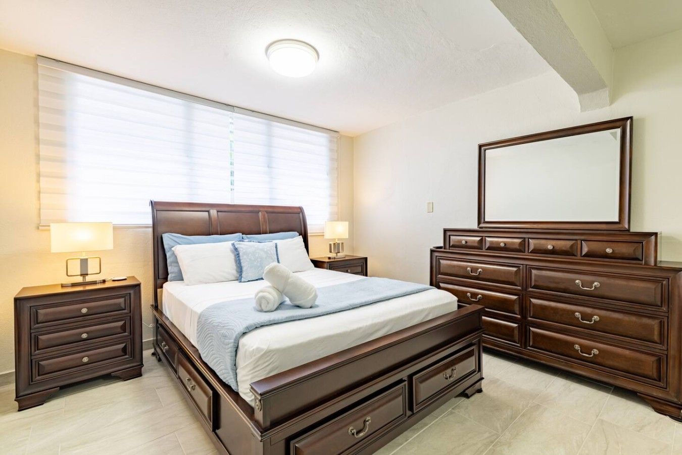 A bedroom with a large bed, a dresser, a mirror, and two bedside tables.