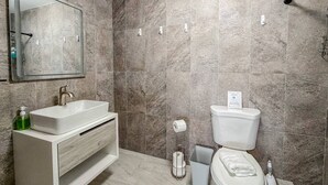 Une salle de bain avec un lavabo blanc, un miroir et des toilettes, des carreaux de marbre et un porte-serviettes.