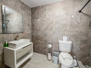 Casa de banho com lavatório branco, espelho e sanita, azulejos de mármore e porta-toalhas.