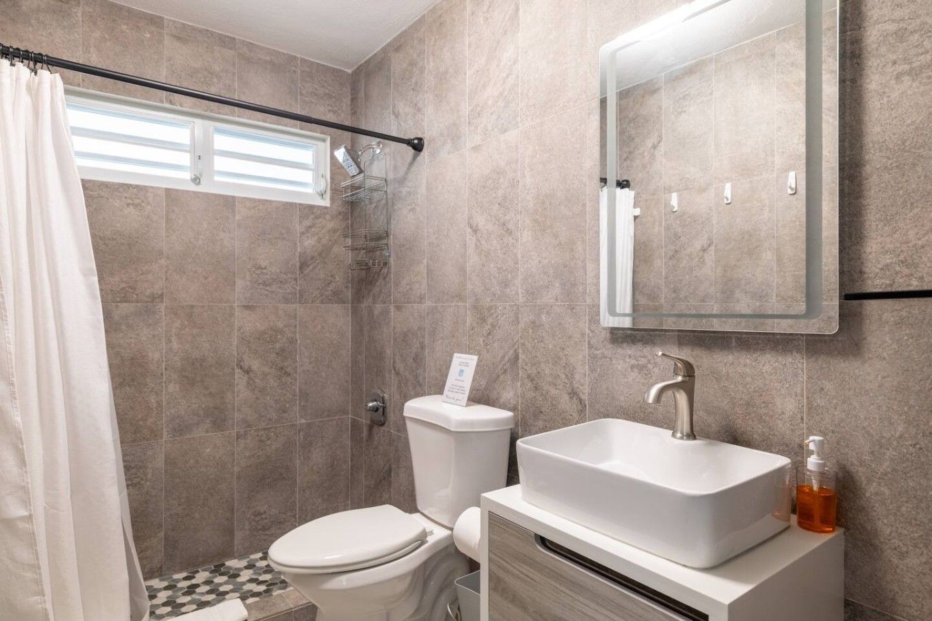 A bathroom with a shower, toilet, sink, and a mirror.