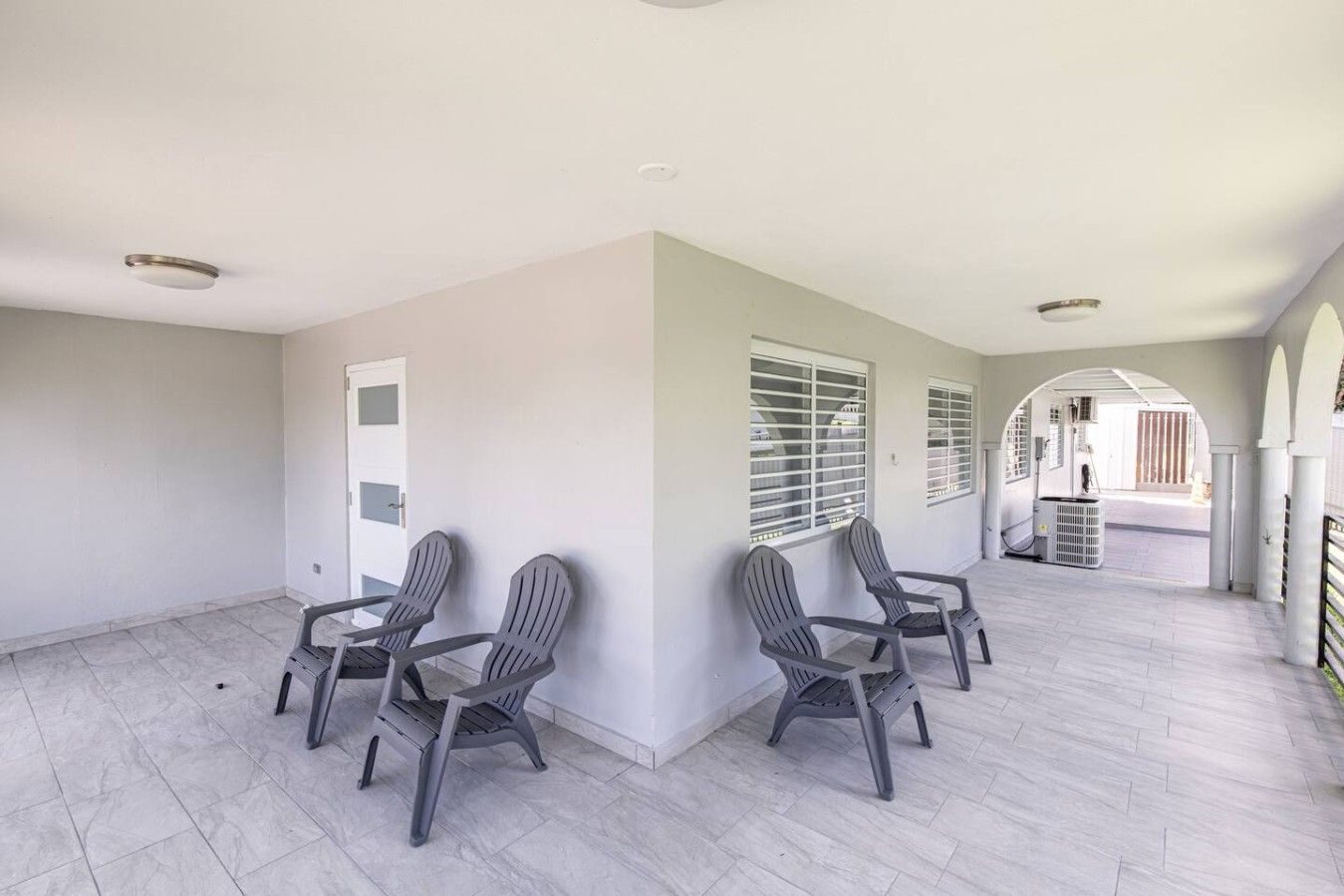 A spacious room with a tiled floor, a door, and a seating area with chairs.