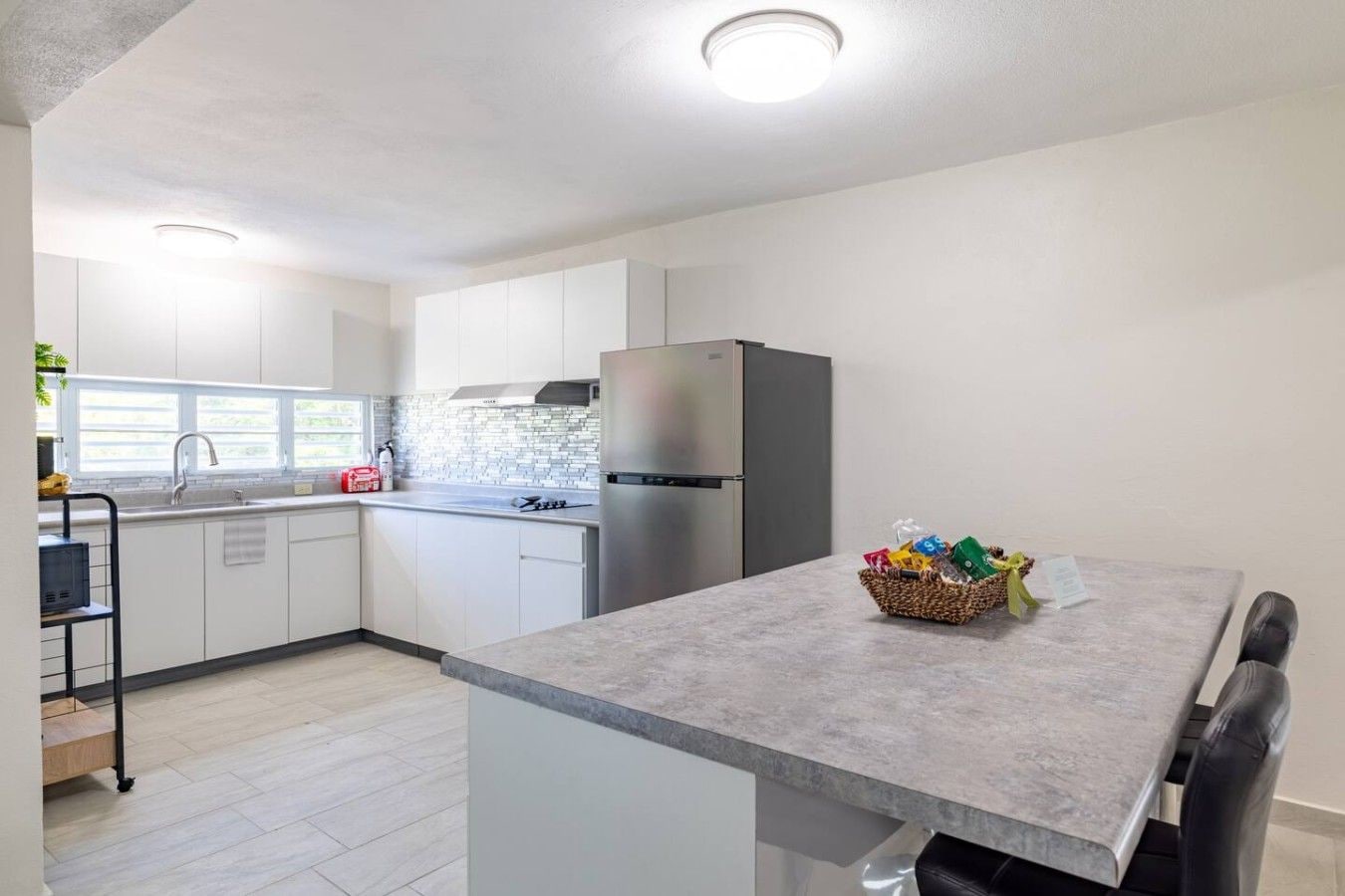 A modern kitchen with white cabinets, a stainless steel refrigerator, and a grey countertop.