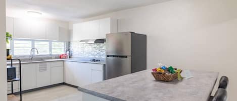 Une cuisine moderne avec des meubles blancs, un réfrigérateur en acier inoxydable et un plan de travail gris.