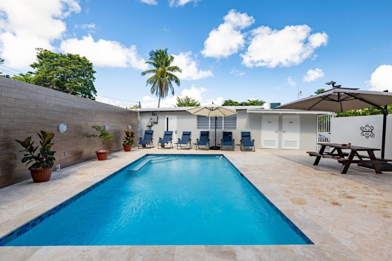 A swimming pool with lounge chairs and a picnic table, surrounded by a brick wall and potted plants.
