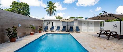 A swimming pool with lounge chairs and a picnic table, surrounded by a brick wall and potted plants.