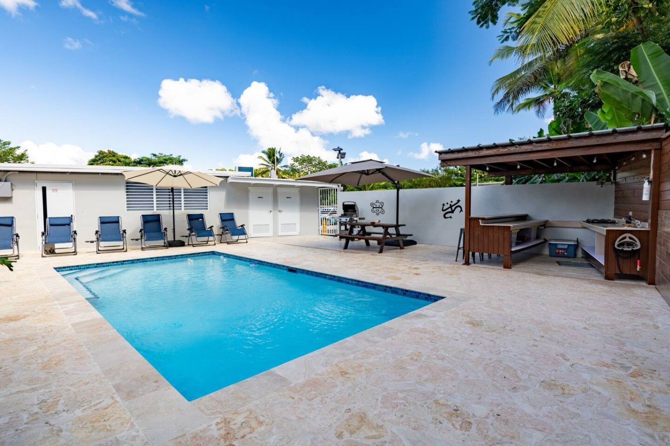 A swimming pool with lounge chairs, a barbecue area, and a covered seating space.