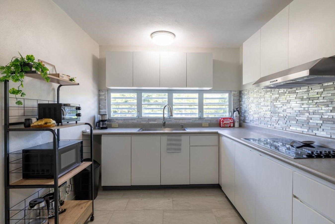 Cozinha moderna com armários brancos, fogão de aço inoxidável e janela com persianas.