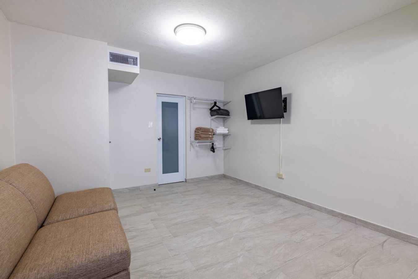 A room with a sofa, a television mounted on the wall, and a door leading to another room.