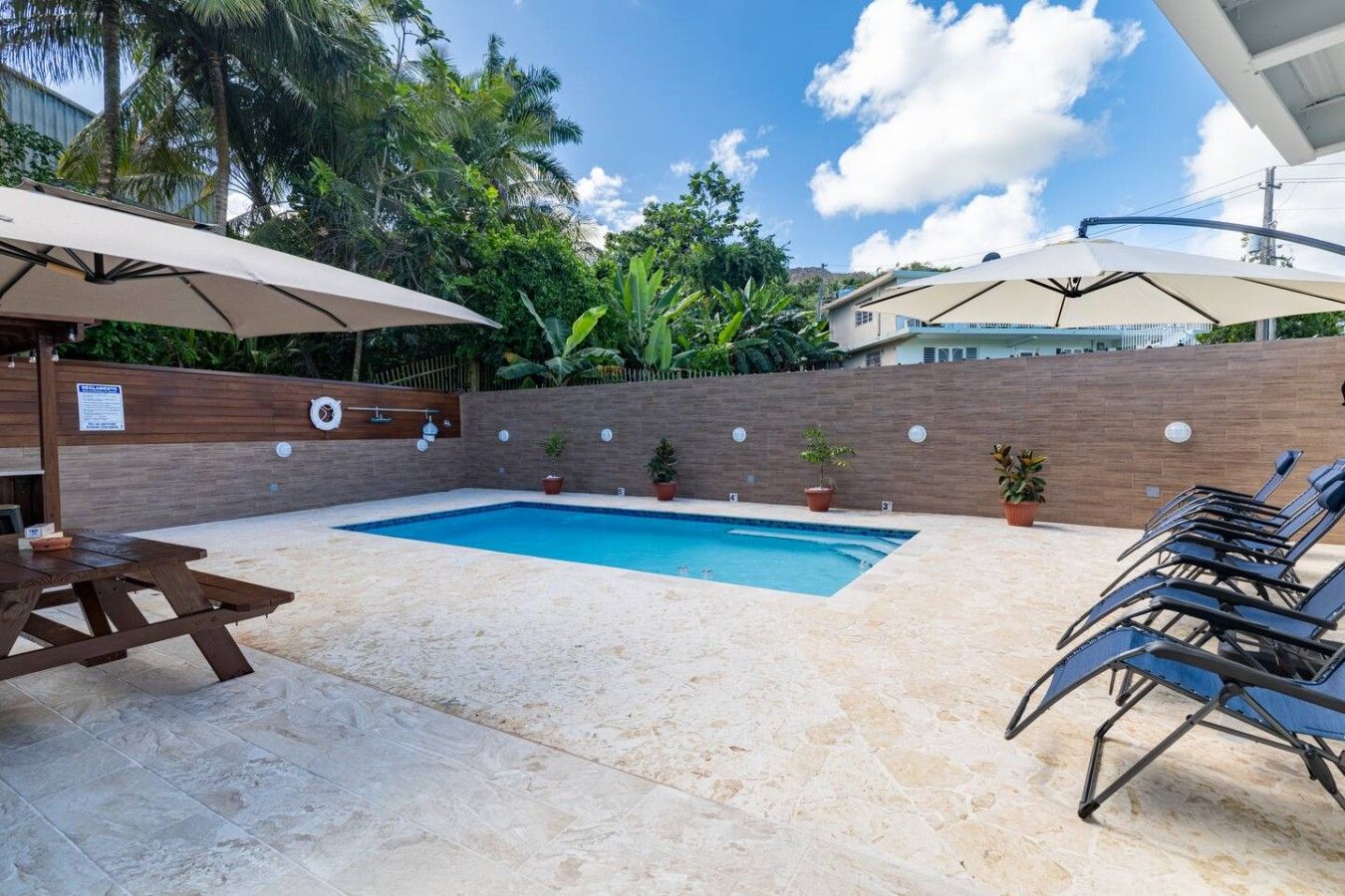 A swimming pool with lounge chairs and umbrellas, surrounded by a brick wall and potted plants.