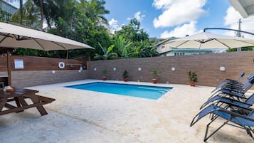 A swimming pool with lounge chairs and umbrellas, surrounded by a brick wall and potted plants.