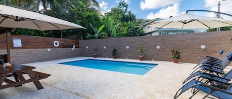 A swimming pool with lounge chairs and umbrellas, surrounded by a brick wall and potted plants.