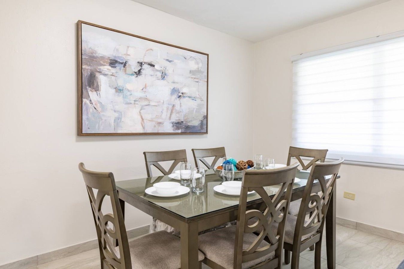 Un comedor con mesa de vidrio, seis sillas y un cuadro abstracto grande en la pared.