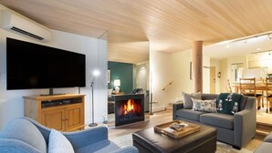 Een moderne woonkamer met een flatscreen televisie, een open haard, een bank en een eethoek.