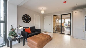 A modern living room with a black leather sofa, a brown ottoman, a small Christmas tree, and a large wall clock. - Modern Entire Home Retreat in Newry (Newry)