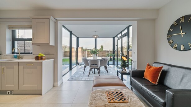 A modern kitchen with a dining area, a black leather sofa, and a large wall clock. - Modern Entire Home Retreat in Newry (Newry)