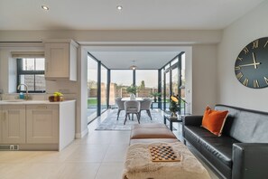 A modern kitchen with a dining area, a black leather sofa, and a large wall clock. - Modern Entire Home Retreat in Newry (Newry)