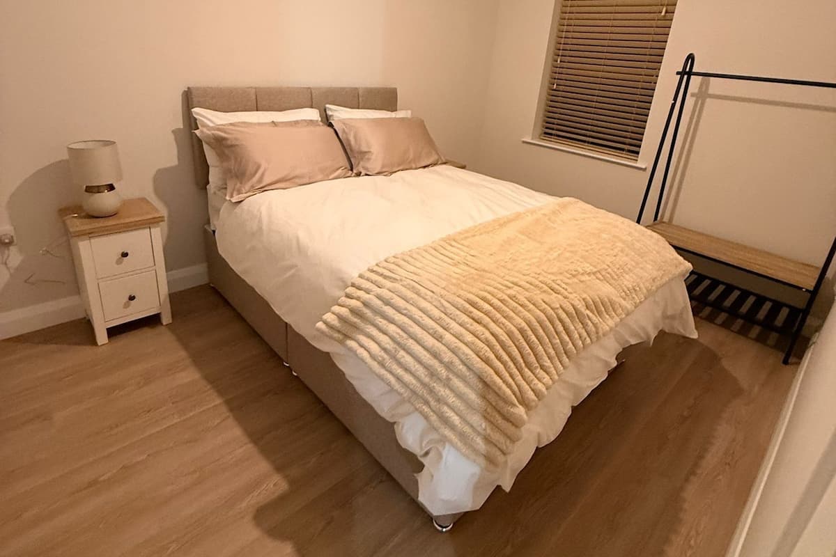 A bedroom with a bed, bedside table, lamp, and a window with blinds.