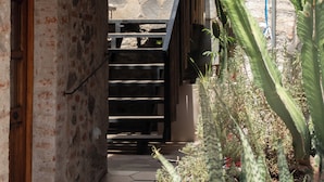 A narrow stone-walled corridor with a wooden door, a metal staircase, and various plants. - Hotel C. Andreu  (San Miguel de Allende)