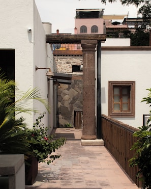 A narrow courtyard with a stone column, a wooden fence, and a door leading to a room. - Hotel C. Andreu  (San Miguel de Allende)