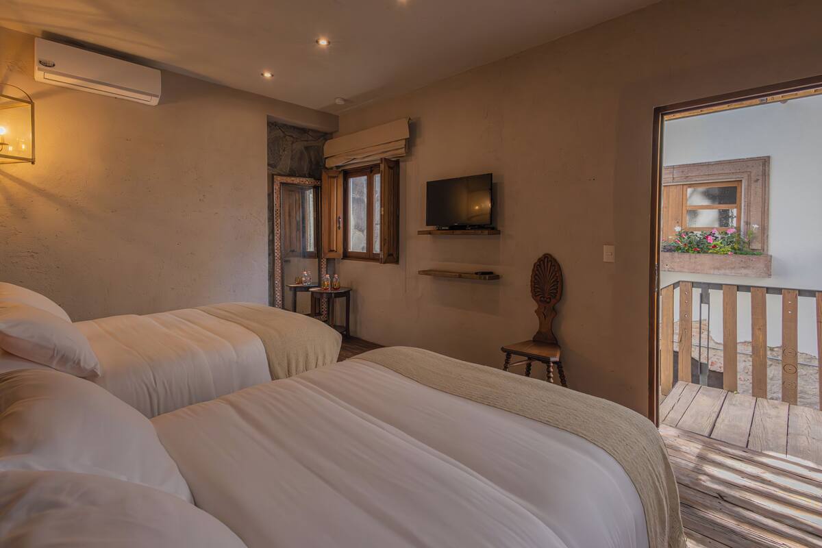A bedroom with two beds, a television, and a balcony with flowers.