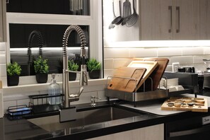 A modern kitchen with a stainless steel sink, a wooden cutting board holder, and a dish rack.