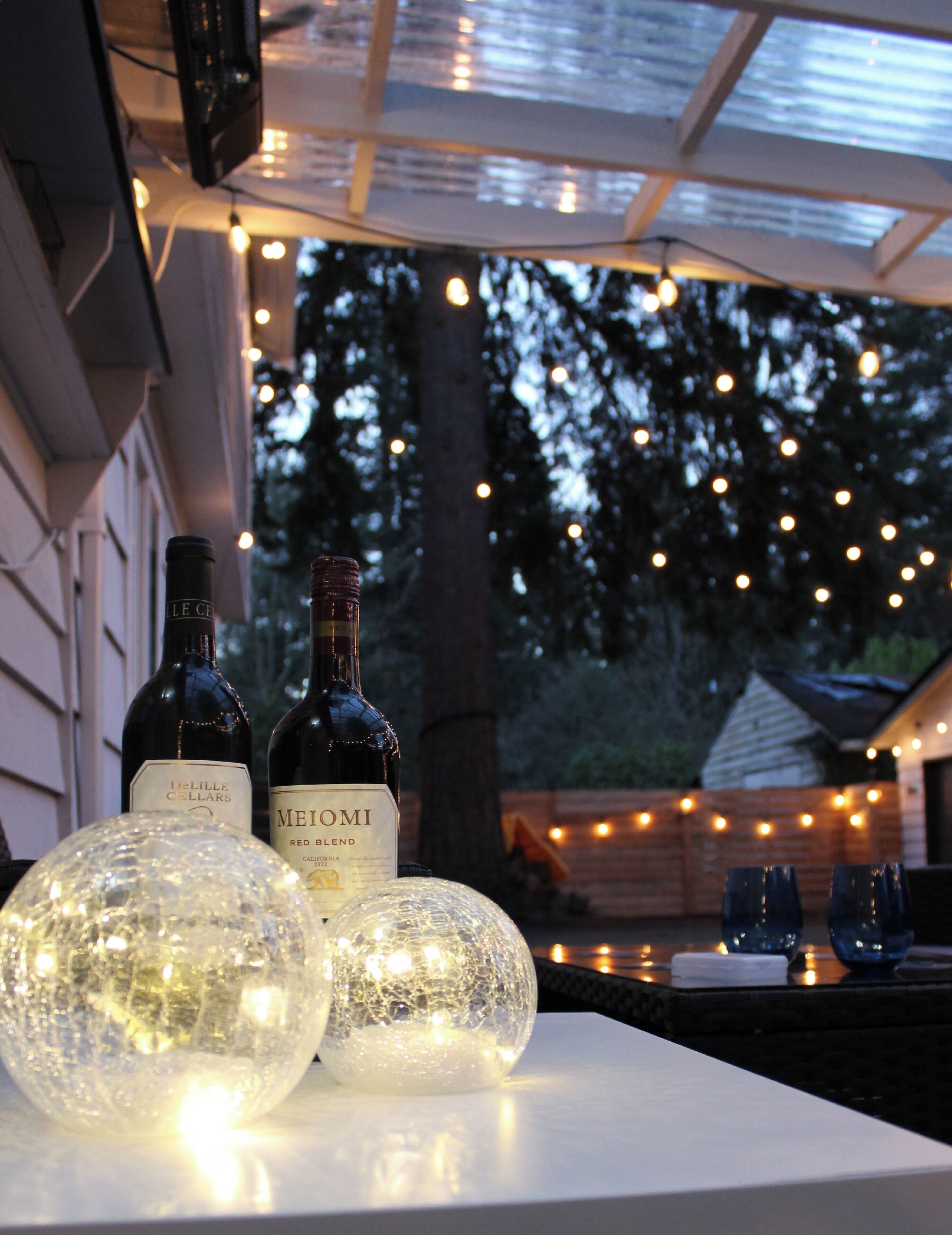 Due bottiglie di vino su un tavolo con sfere di vetro decorative e luci a stringa sullo sfondo.