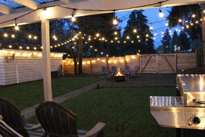 An outdoor patio area with string lights, a fire pit, and a grill.