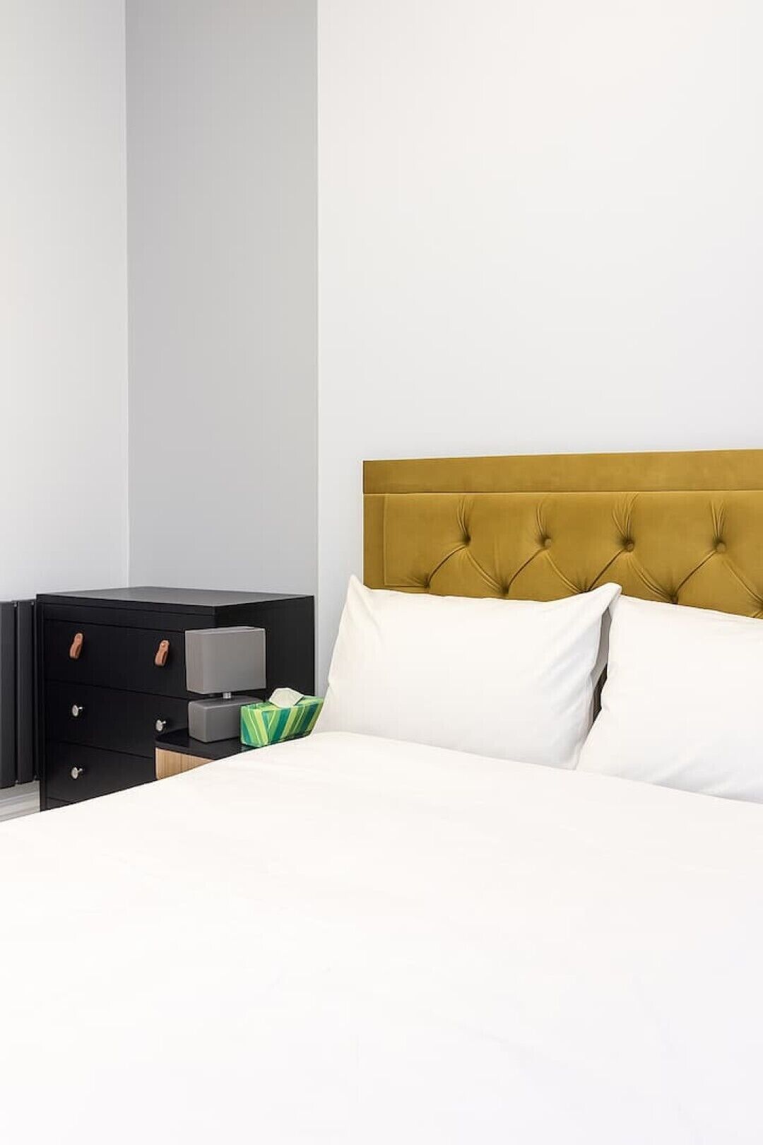 A bed with a tufted headboard, a bedside table with drawers, and a lamp.