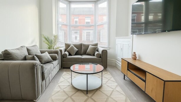 A living room with a sofa, a coffee table, and a TV mounted on the wall.