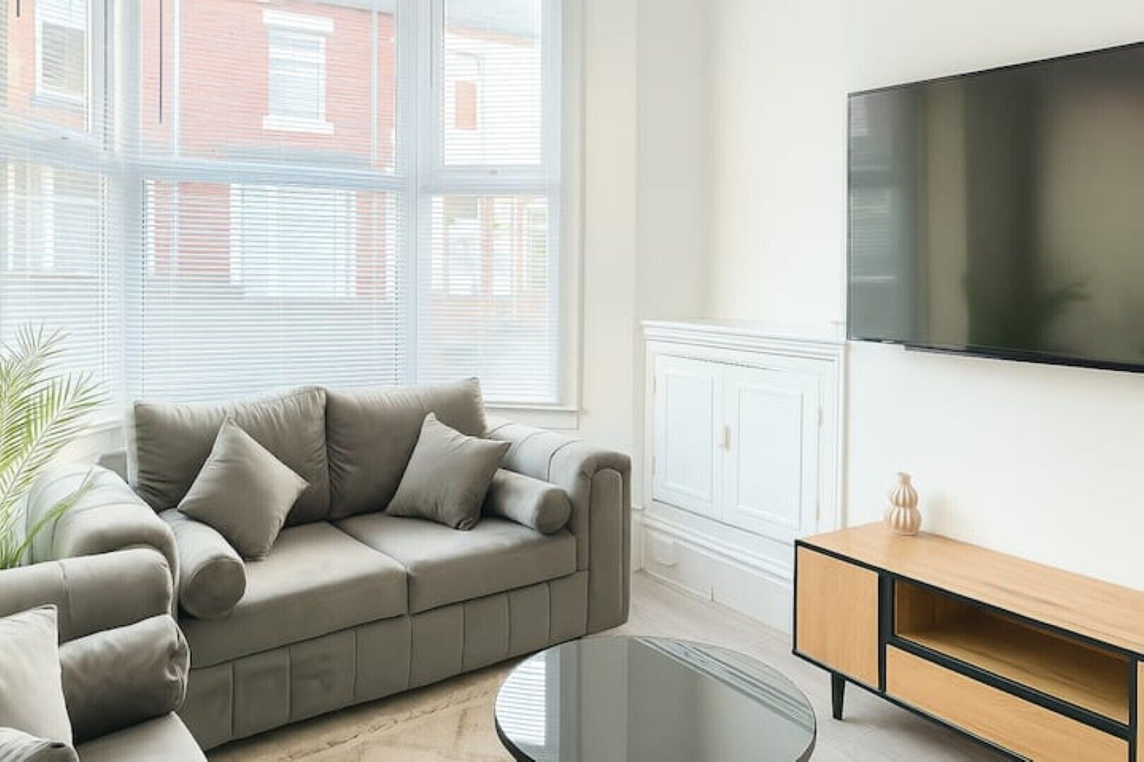Una sala de estar moderna con un sofá color beige, una mesa de centro de vidrio y un mueble de televisión de madera.