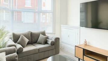 Una sala de estar moderna con un sofá color beige, una mesa de centro de vidrio y un mueble de televisión de madera.