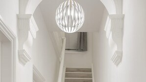 A staircase with a wooden finish, white walls, and a modern pendant light.