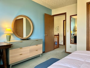Ein Schlafzimmer mit Bett, Schminktisch, Spiegel und einer Tür zu einem anderen Raum.