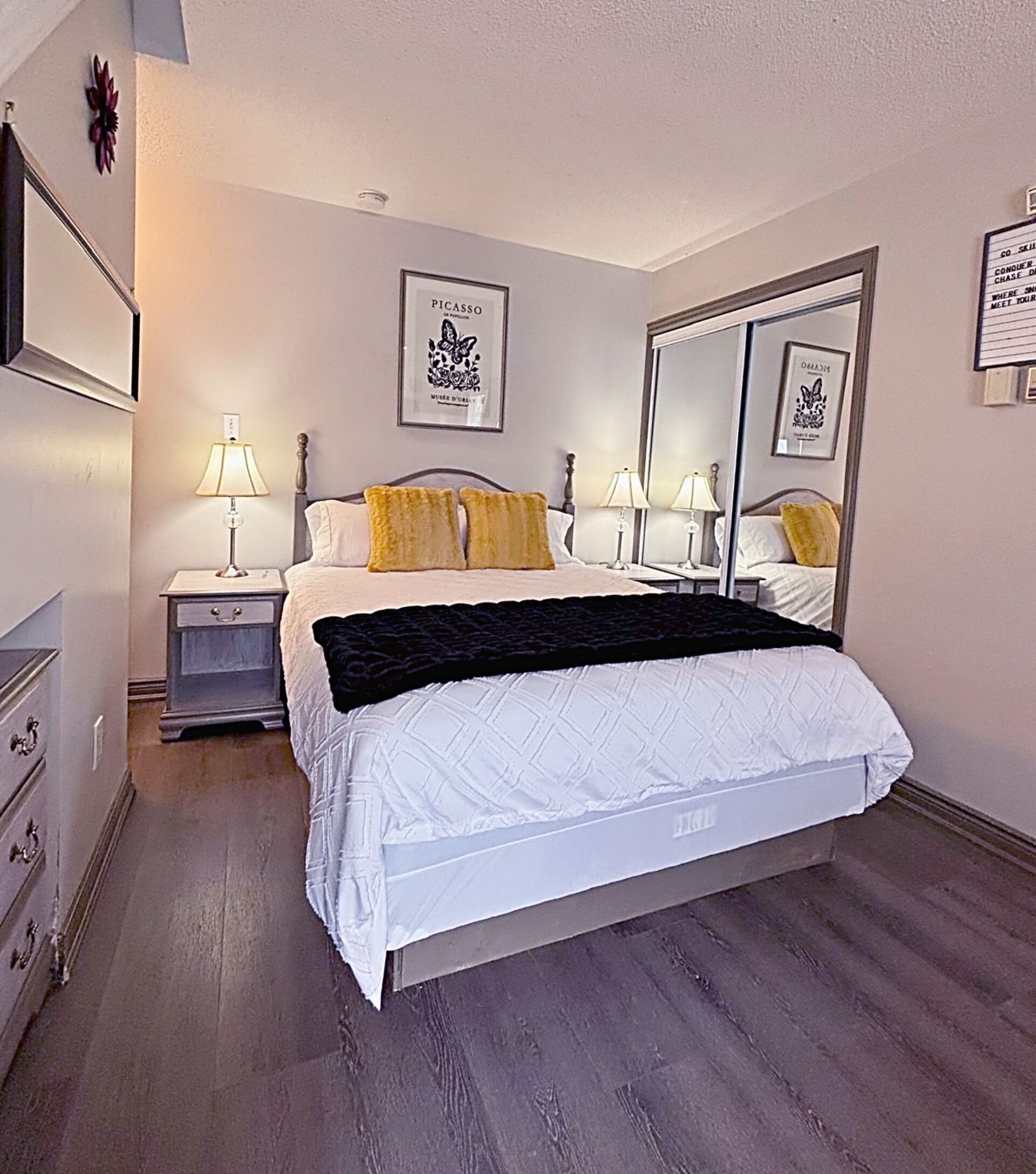 Un dormitorio con una cama, dos mesitas de noche con lámparas, un aparador y un espejo grande.
