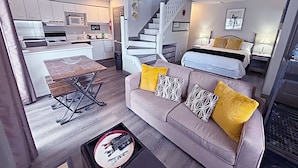 A compact living space with a kitchenette, a sofa with patterned cushions, a dining table, and a staircase leading to an upper level. - Slopeside Loft at North Creek Resort  (The Blue Mountains)