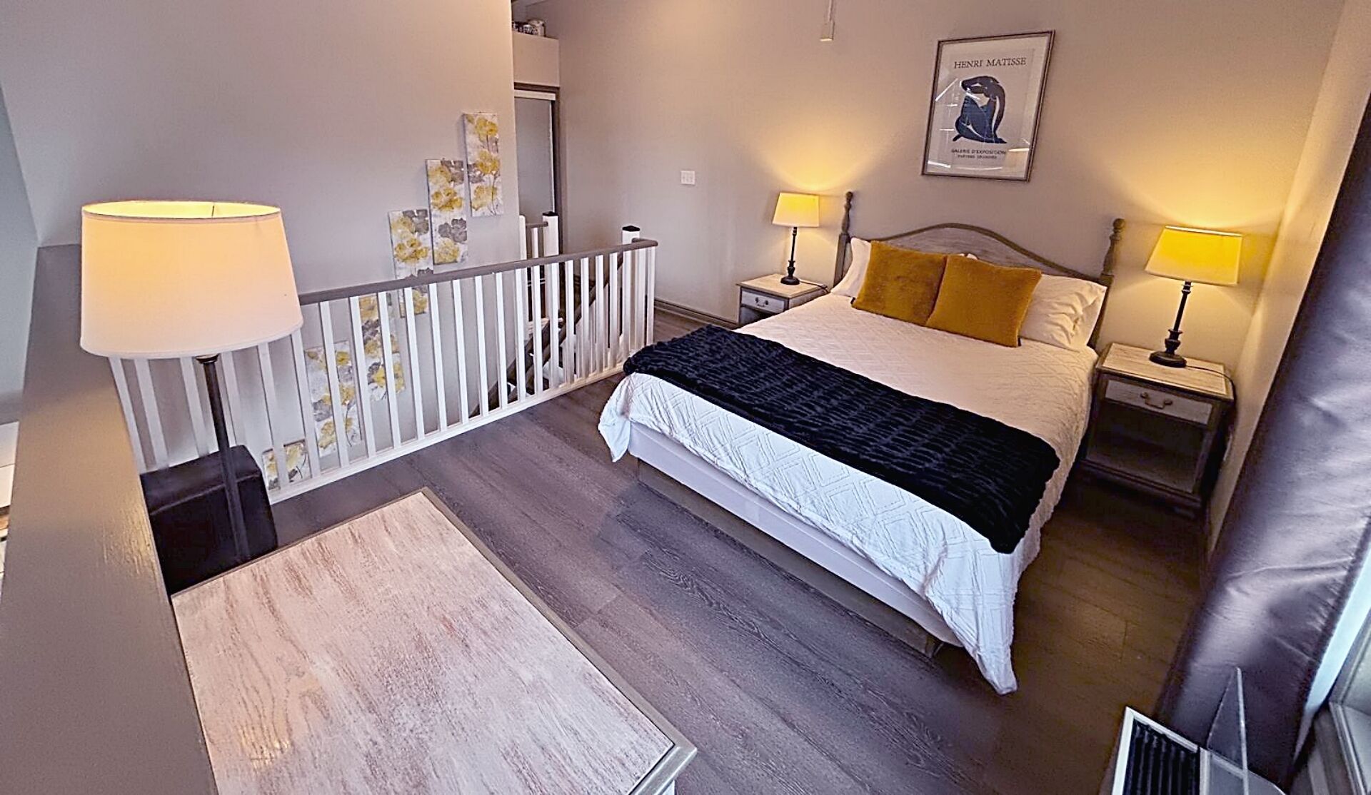 Une chambre à coucher avec un lit, deux tables de chevet, une commode, une balustrade blanche et un tableau au mur.