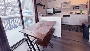 A compact kitchen with a central island, a dining table, and a view through a sliding glass door. - Slopeside Loft at North Creek Resort  (The Blue Mountains)
