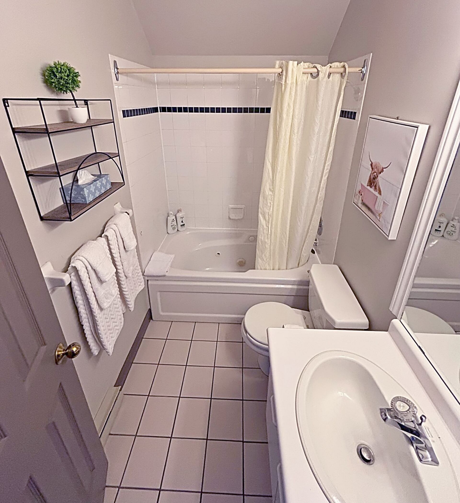 Une salle de bain avec une baignoire, des toilettes et un lavabo. On y trouve un porte-serviettes avec des serviettes, une petite plante en pot et un tableau encadré accroché au mur.