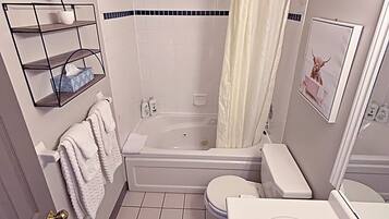 Une salle de bain avec une baignoire, des toilettes et un lavabo. On y trouve un porte-serviettes avec des serviettes, une petite plante en pot et un tableau encadré accroché au mur.