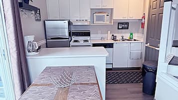 Una cocina compacta con gabinetes blancos, microondas, estufa y refrigerador.